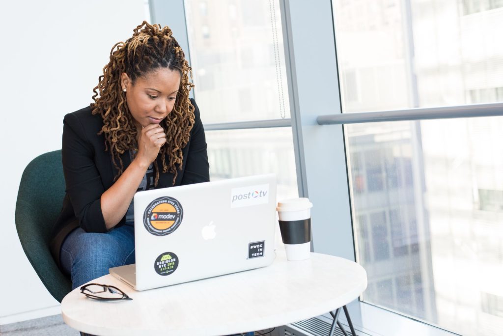 Femme avec des dreadlocks concentrée sur un ordinateur portable à un bureau avec vue sur la ville.
