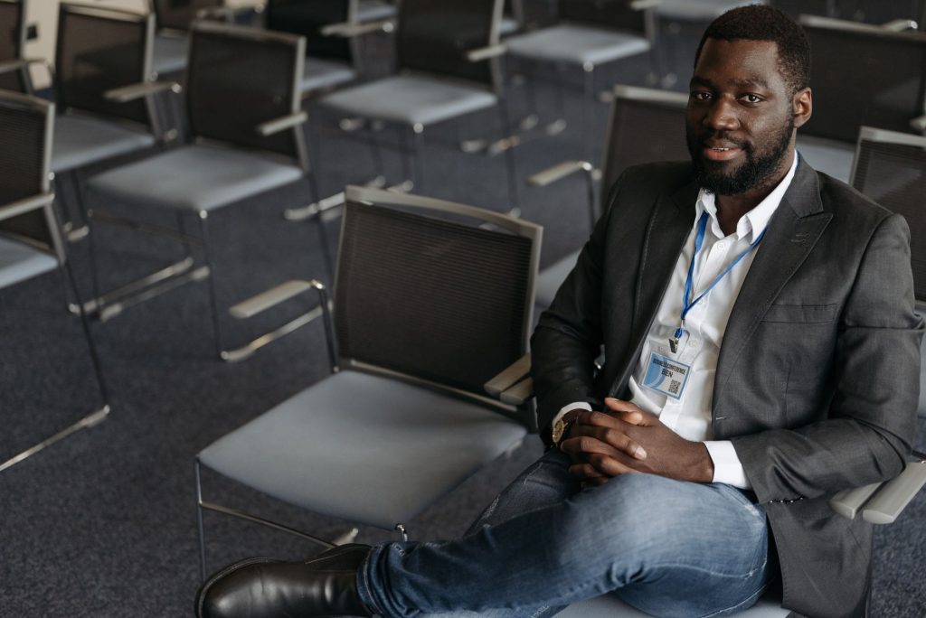 Homme d'affaires assis avec confiance dans une salle de conférence moderne, souriant avec un badge.