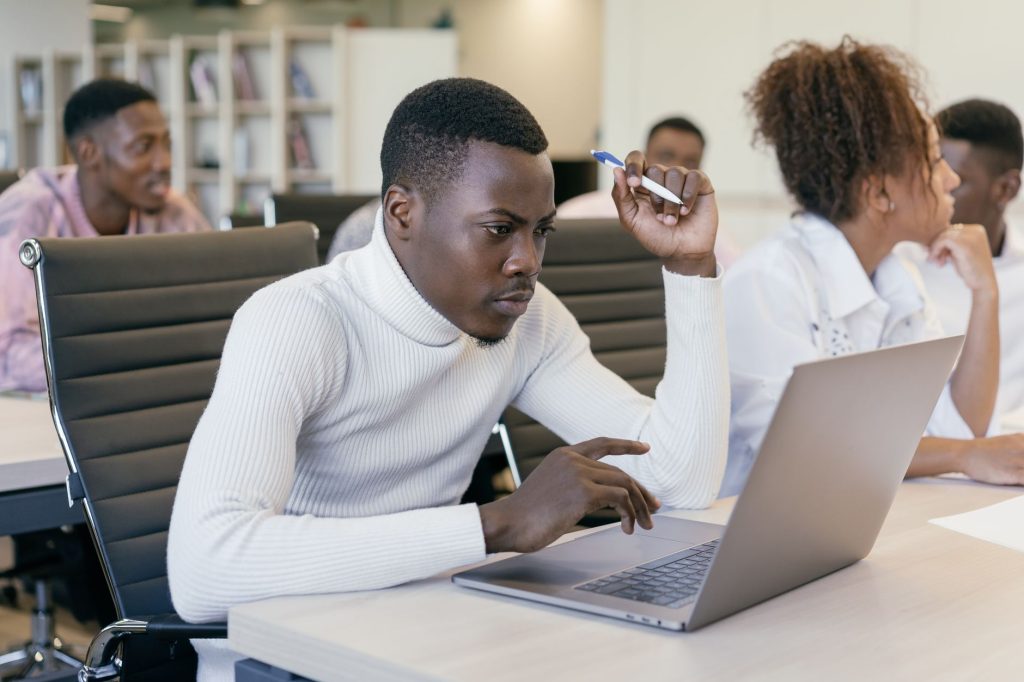 Jeune homme travaillant avec attention sur un ordinateur portable dans un cadre de bureau, se concentrant sur sa tâche.