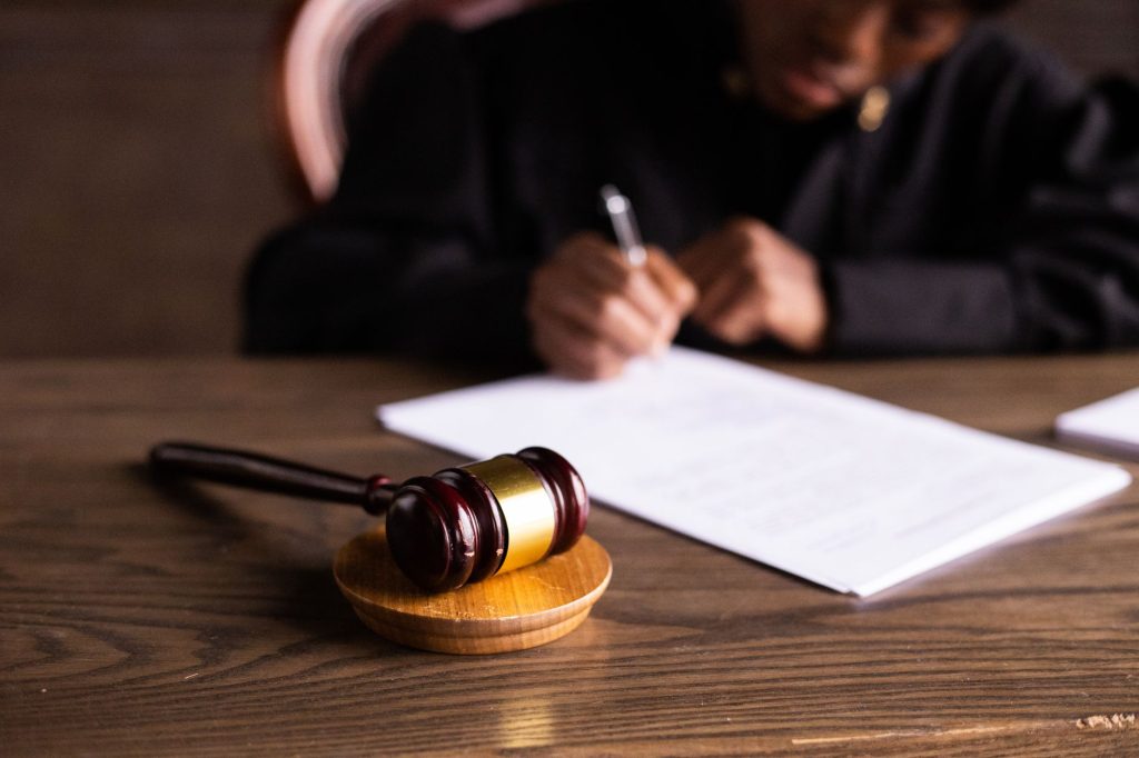 Juge signant des documents sur un bureau avec un accent sur le maillet, représentant la loi et la justice.