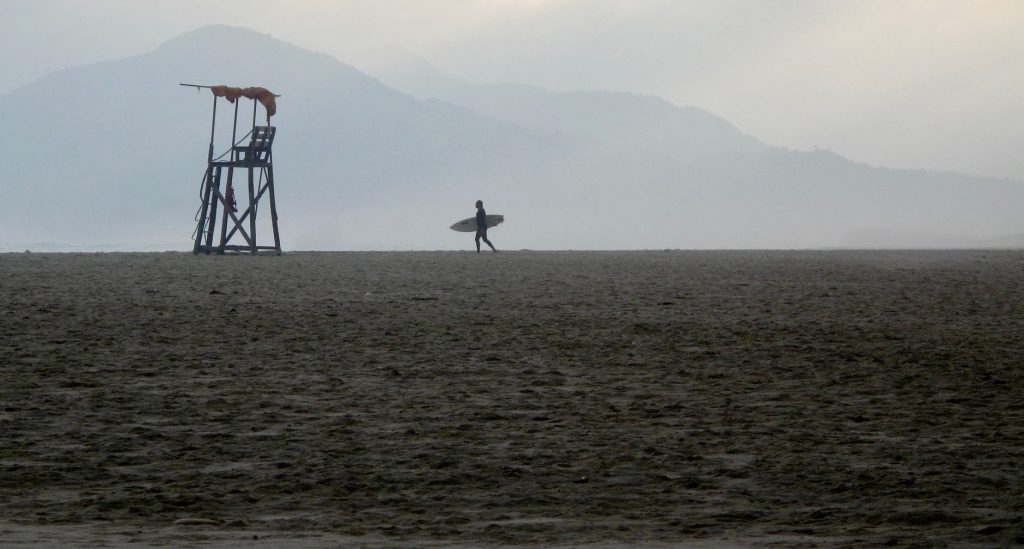 Silhouette d'un surfeur marchant sur une plage brésilienne près d'un poste de secours à l'aube.