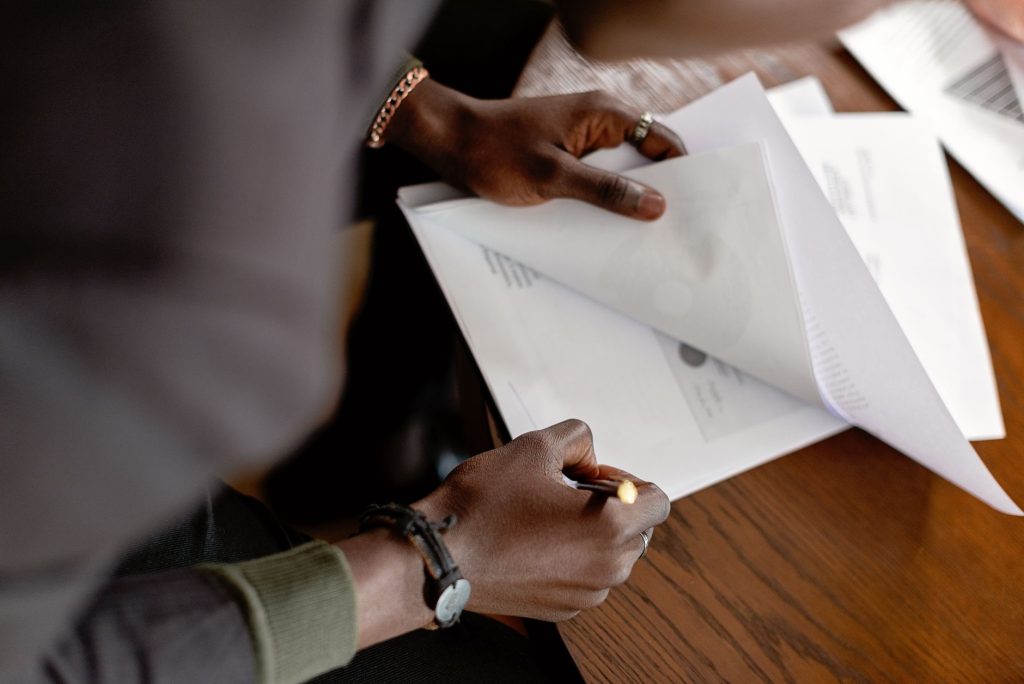 Un adulte afro-américain révisant des papiers avec un crayon à un bureau, mise au point sur les mains et les documents.