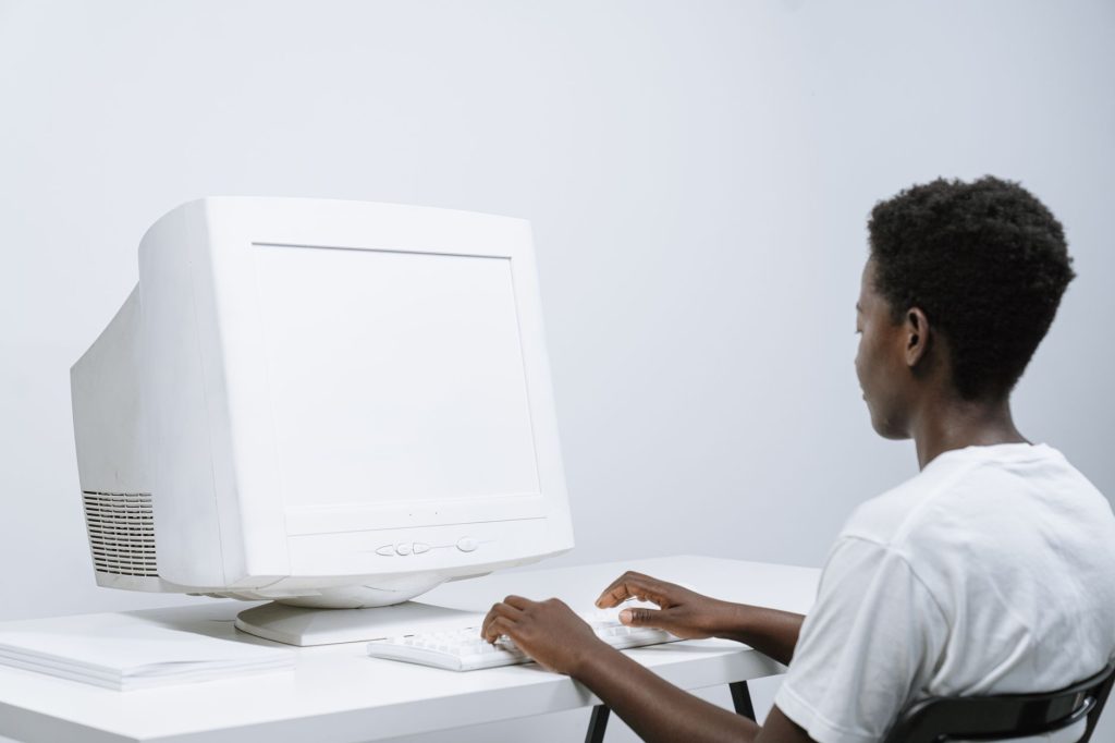 Un homme adulte tapant sur un moniteur CRT blanc dans un bureau moderne et minimal.