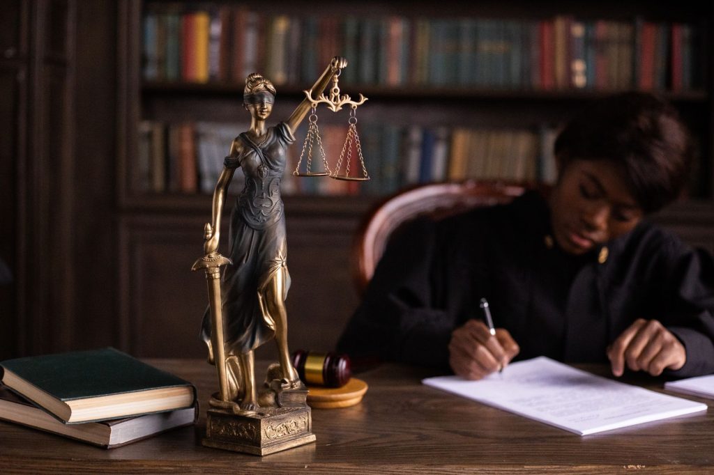 Un juge concentré écrivant sur des documents à côté d'une statue de la Justice dans un bureau.